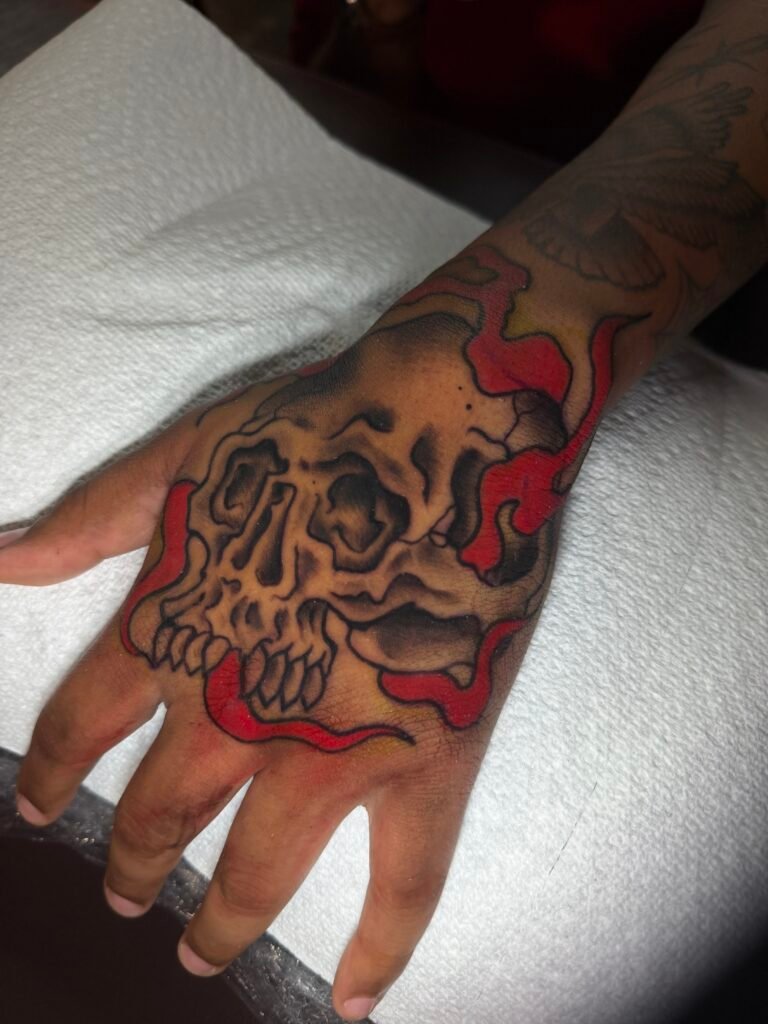 Black and grey skull tattoo with red flames across the hand